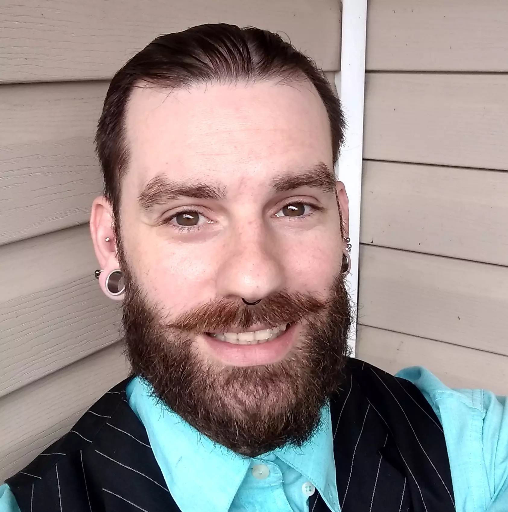 A web developer, named Tucker Wray, on his balcony wearing a turquoise shirt and a striped vest.